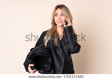 Russian girl with a motorcycle helmet isolated on beige background holding coffee to take away and a mobile