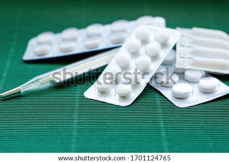Convalutes with tablets and a thermometer on a green background