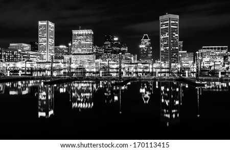 The skyline and docks reflecting in the water at night, in the Inner Harbor of Baltimore, Maryland.