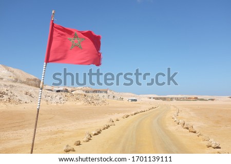 Desert Road with Moroccan Flag in Western Sahara Leading to Tourist Resort Royalty-Free Stock Photo #1701139111