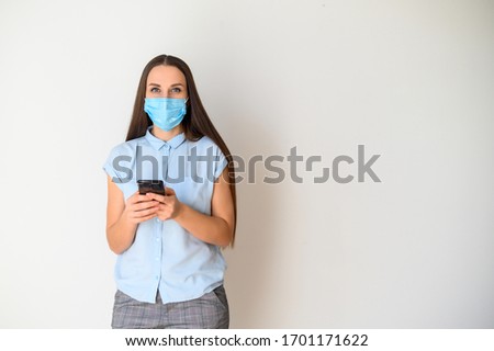 Protect yourself from epidemic, communicate remotely. A young woman in a medical mask on her face is chatting on a smartphone, she is typing a message. Isolated on a white background.