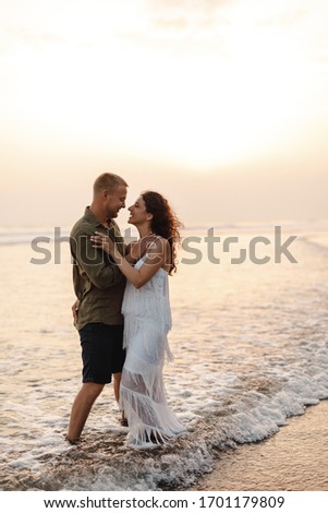 Couple kissing on the beach with a beautiful sunset in background, wavws touch ther feets. Honeymoon concept