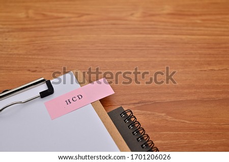 The words "HCD" written on sticky note with clipboard in diagonal angle.