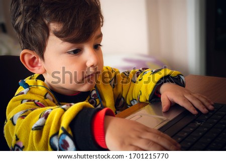 3 years old curious Turkish baby wearing yellow pajamas playing games with laptop