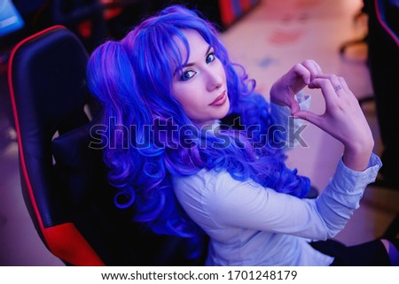Streamer anime cosplay woman shows heart sign with hands professional gamer playing online video games computer, neon color.