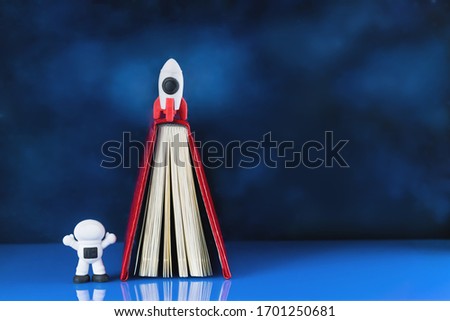 concept of success with toy rocket in the sky and astronaut and a book or diary as launching platform. Cosmonautics Day. Creativity and thinking outside the box, growth and development. Copy space