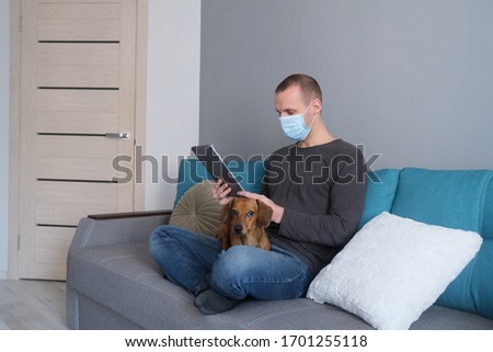 Man wearing mask with a dog on the sofa. Concept of corona virus quarantine. Working and staying at home.