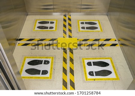 View of footprint sign for stand in lift. Social distancing with COVID-19 coronavirus crisis. yellow footprint sign with text caution social distance, Social distancing the elevator (Lift) in hotel.