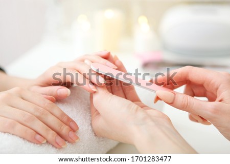 Closeup shot of a woman in a nail salon getting a manicure by a cosmetologist with a nail file. Woman gets a manicure of nails. Beautician puts nails on the client.
 Royalty-Free Stock Photo #1701283477