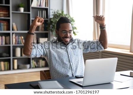 Overjoyed African American male worker sit at office desk feel euphoric read good business news on laptop, excited biracial man triumph win lottery online on computer, reward, luck concept Royalty-Free Stock Photo #1701296197