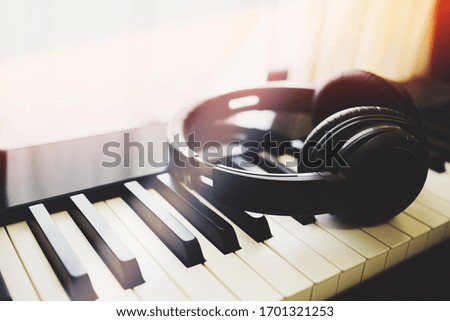 Music headphone on piano keyboard with rim light from the window. Vintage filter. Music and entertainment concept.