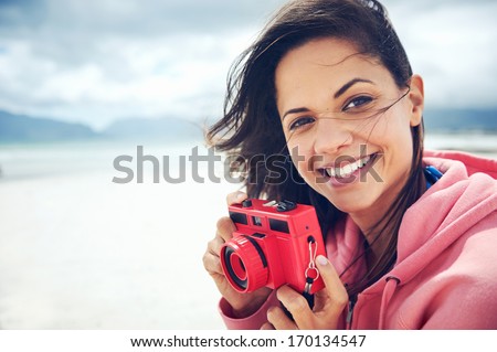 Portrait of beautiful Latino woman with retro hipster camera having fun at the beach