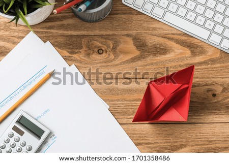 Businessman workspace at office desk with red paper ship. Top view office workplace background. Flat lay table with computer keyboard, calculator, business reports and pen. Main project management
