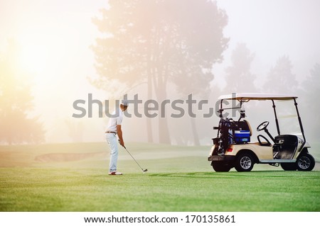 Golfer lining up shot with iron club on golf course in fairway at sunrise