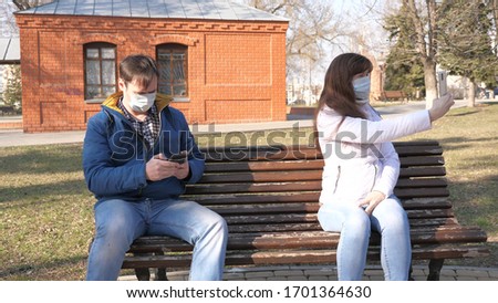 Coronavirus protection. woman and man in medical protective mask are sitting with smartphone on city street in Europe. Tourists on street wear a protective mask from viruses selfies on smartphone.