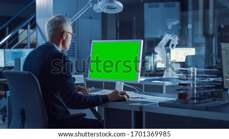 Professional Heavy Industry Engineer Works on Green Mock-up Screen Computer. Engineering Bureau and Industrial Design Agency with Various Robotic, Architectural and Machinery Components