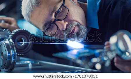 Close-up Portrait of Focused Middle Aged Engineer in Glasses Working with High Precision Laser Equipment, Using Lenses and Optics for Accuracy Electronics. Testing Superconductor Material Royalty-Free Stock Photo #1701370051