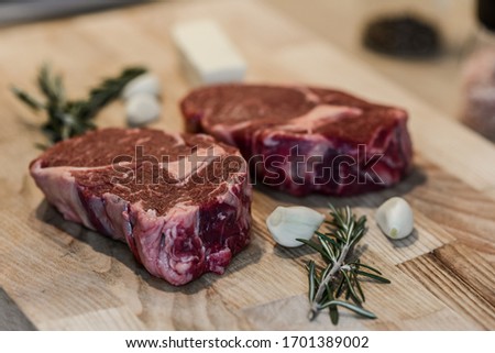 Dry-aged raw meat steak on a wooden plate with herbs and garlic. Close up raw meat beef cut on a wooden chopping board with garlck, thyme and butter.Selective focus. Clean background natural lightning