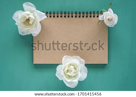 White roses and blank notebook paper on emerald background.