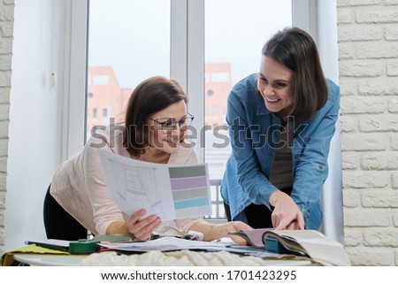 Two women designers working with fabric samples for interior. Choosing fabrics for curtains, furniture upholstery, calculating cost