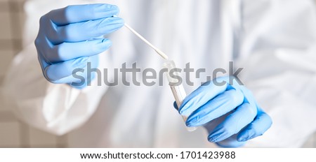 Doctor holding swab test tube for 2019-nCoV analyzing. Coronavirus test. Blue medical gloves and protective face mask for protection against covid-19 virus. Coronavirus and pandemic. Royalty-Free Stock Photo #1701423988