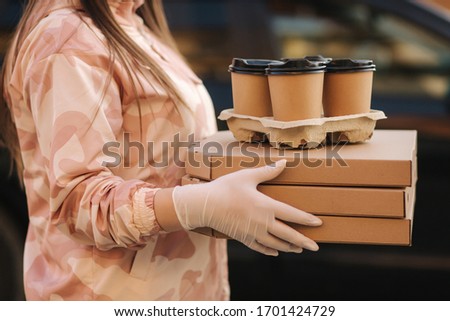 Young woman in protective mask and medical mask take order from delivery boy outside. Food delivery in quarantine. Courier bring Pizza and coffee for customer