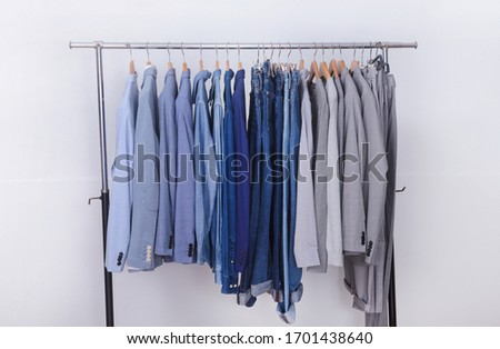 Men’s row of blue ,gray suit with long sleeve blue,white ,jeans shirt and blue jeans and gray pants on hanger
