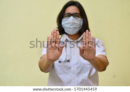 Portrait of young medical health care female worker showing her hands out, wearing surgical face mask to protect from Corona Virus (COVID-19) pandemic against yellow background.Concept Ready to fight
