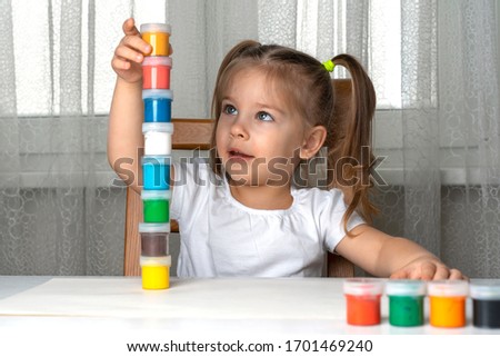 a girl in quarantine sits and builds a tower of paint cans, has found new jars and is preparing to build higher