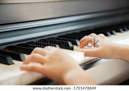 Close up of a little student's hands is playing, learning and practicing the piano. Piano chords In the key of C major. Music abilities for kids. Hobby and activity for the children. Selective focus. Royalty-Free Stock Photo #1701478849