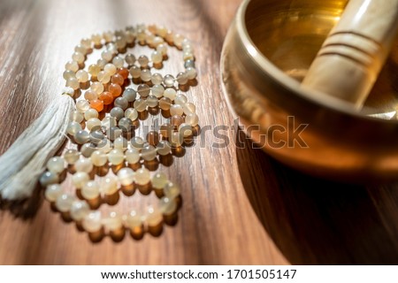 Handmade sacred mala seed beads and a golden Tibetan bowl on a wooden background in the soft and beautiful light of morning, a perfect time for a yoga session acompanied by healing sounds. Royalty-Free Stock Photo #1701505147