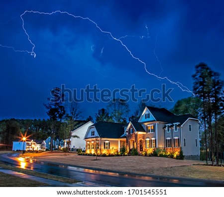 Powerful lightning storm front passes over residential houses, focus on the house, long exposure