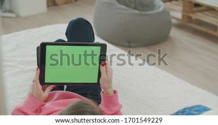 View over head on of caucasian woman lying on the bed at home. Girl holding tablet computer with green screen while watching something. Chroma key. 
