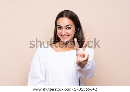 Young telemarketer woman over isolated background smiling and showing victory sign