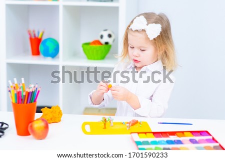 Little beatiful schoolgirl  is sitting at the desk with colorful plastic