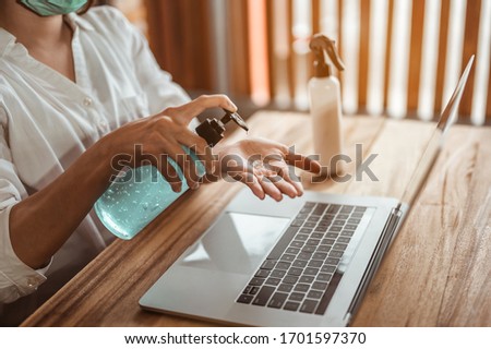 Office worker working from home during coronavirus outbreak cleaning her hands with sanitizer gel and wearing protective mask. Coronavirus, covid-19, Work from home (WFH), Social distancing concept. Royalty-Free Stock Photo #1701597370