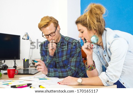 Two colleagues working together on an innovative product design in a creative studio behind a desk, littered with markers, sketches, drawings and 