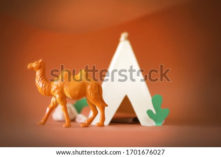 A camel walks in the desert in the heat of the day behind it a mountain and a Bedouin tent and vegetation and sand, a strong summer sun