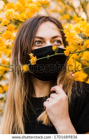 a girl in black medical mask near the tree with yellow flowers