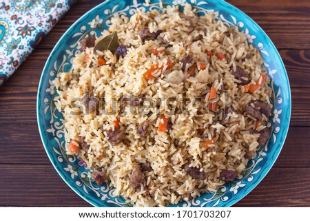 National cuisine - Uzbek pilaf with meat in a plate with a traditional pattern, on a dark wooden table. Dastarkhan. Navruz concept