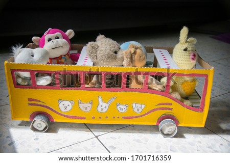 Homemade bus for kids, made of cardboard, painted yellow, with dolls as passengers. 