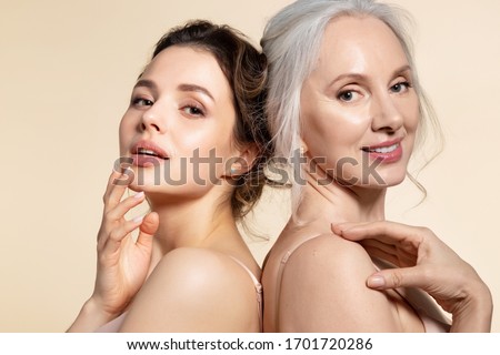 Two beautiful different age woman with perfect skin headshot portrait. Senior lady and young girl in underwear standing back-to-back posing for camera. Spa beauty salon procedure and home skincare Royalty-Free Stock Photo #1701720286