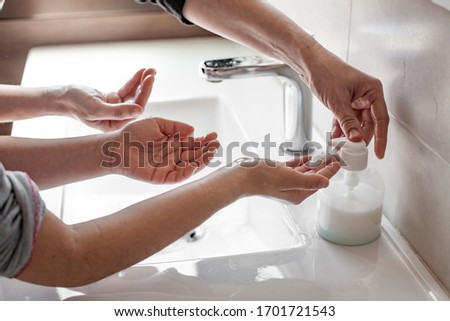 Mother teaching her daughter how to properly wash their hands with soap to prevent coronavirus infection