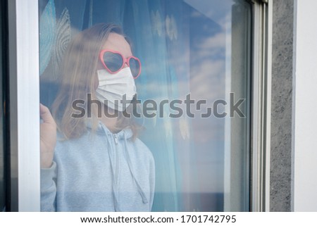 Covid-19 self-isolation. Female looking through window, Wearing mask and red love heart shape sunglasses. Hope and stay at home message. Closeup portrait