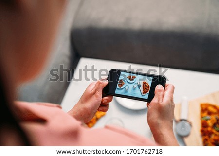 Woman making a photo with smartphone of a Italian homemade pizza on the living room table