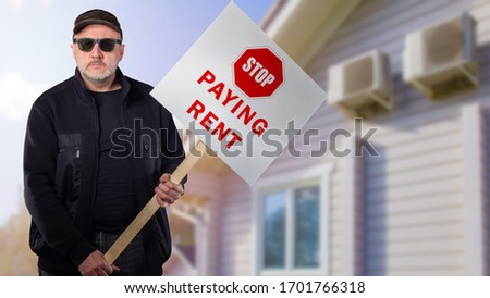 Sad man with a sign Stop paying rent on the background of the house. People put forward economic demands. The man draws attention to the difficult situation of mortgage borrowers.