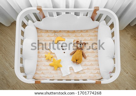 Baby romper with toy bear for a newborn in cot, cradle.  White wooden baby crib with pillows shaped clouds  in baby's room. Top view of child's bed Royalty-Free Stock Photo #1701774268