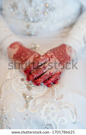 Pair of hand of a beautiful young bride with mehndi/heena design with white wedding gown.