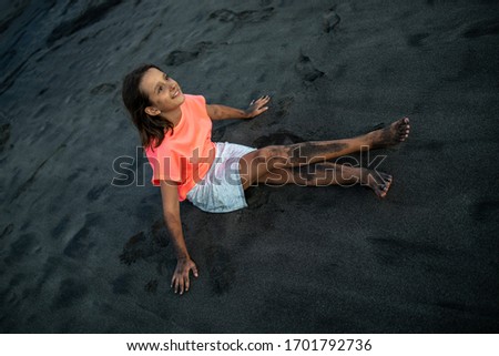 A little girl in a bright red t-shirt is lying on the beach of Bali.