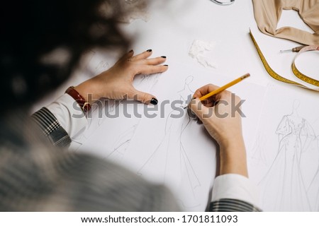 Close-up of work process of a fashion designer at her studio. Drawing sketch of of dress /gown. Bridal fashion designer.